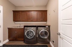 Rich wood-finish cabinetry, integrated utility sink, stone-finish countertop, and tile flooring - 
