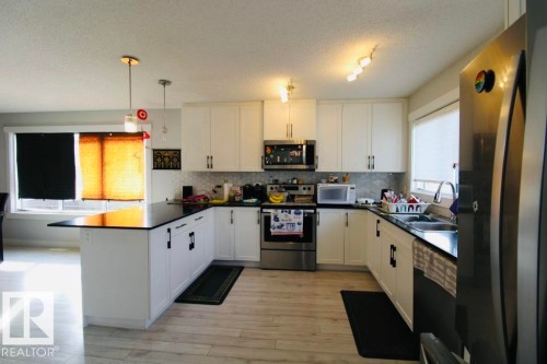 Kitchen with white cabinetry, black countertops, stainless steel appliances, and wood-finish flooring - 17440 77 Street Nw, Edmonton, AB 