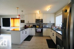Kitchen with white cabinetry, black countertops, stainless steel appliances, and wood-finish flooring - 