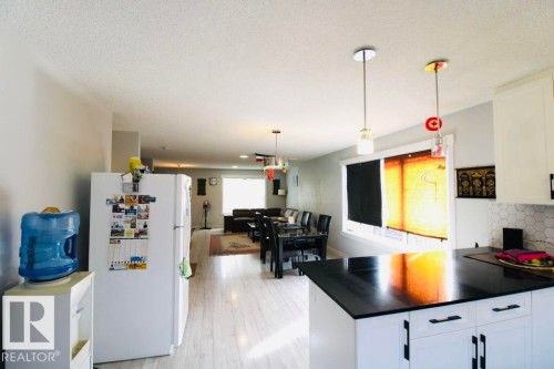 Open-concept interior featuring light wood-finish flooring, white cabinetry, dark countertops, and a hexagonal tile backsplash - 17440 77 Street Nw, Edmonton, AB 
