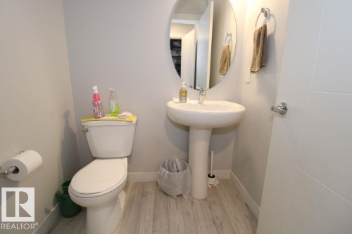Pedestal sink with a round mirror, light wood-finish flooring, and a white toilet - 17440 77 Street Nw, Edmonton, AB 