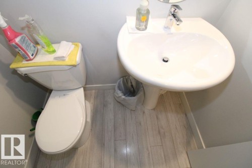 Pedestal sink with chrome faucet, light-toned wood-finish flooring, and a white toilet - 17440 77 Street Nw, Edmonton, AB 