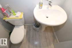Pedestal sink with chrome faucet, light-toned wood-finish flooring, and a white toilet - 