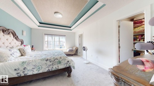 Recessed tray ceiling with light fixture, carpeted flooring, built-in closet with shelving, and large window with blinds - 1103 30 Street Nw, Edmonton, AB 