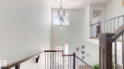 Two-story foyer featuring an ornamental chandelier, upper transom window, and dark wood-finish staircase with wrought iron balusters - 