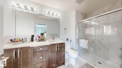 Dual-sink vanity with wood-finish cabinetry, light-toned countertops, and a large wall-mounted mirror - 1103 30 Street Nw, Edmonton, AB 