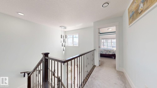 Staircase with dark wood newel posts and wrought iron spindles, contemporary chandelier, recessed ceiling lighting, multi-pane window, and carpeted hallway - 1103 30 Street Nw, Edmonton, AB 