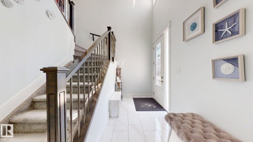 Entryway featuring a two-story ceiling, a staircase with wood newel posts and handrails, carpeted treads, and tile flooring - 1103 30 Street Nw, Edmonton, AB 