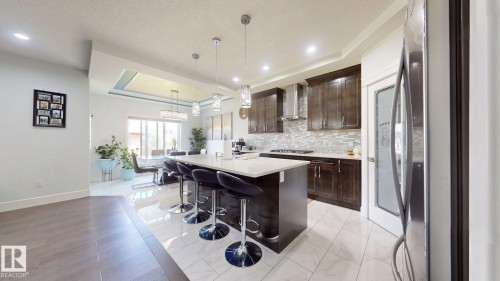Kitchen featuring a central island with counter seating, stainless steel appliances, dark wood-finish cabinetry, and a textured tile backsplash - 1103 30 Street Nw, Edmonton, AB 