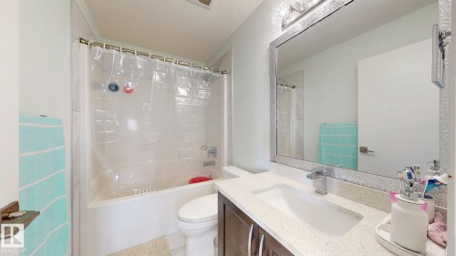 White bathtub and shower combination with a chrome showerhead, a single vanity with a rectangular sink, a light-toned countertop, and a vanity mirror with an illuminated fixture - 1103 30 Street Nw, Edmonton, AB 