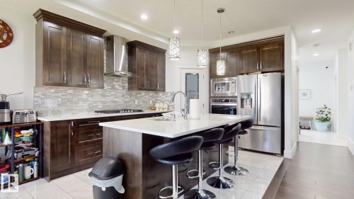 Kitchen featuring rich wood cabinetry, stainless steel appliances, a center island with countertop seating, and a mosaic tile backsplash - 1103 30 Street Nw, Edmonton, AB 
