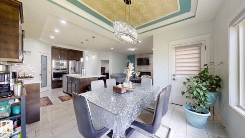 Open-concept kitchen and dining area featuring a tray ceiling with decorative paneling, built-in stainless steel appliances, a large kitchen island, and tiled flooring - 1103 30 Street Nw, Edmonton, AB 