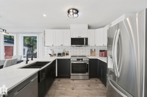 Modern kitchen featuring a dual-tone cabinetry, stainless steel appliances, durable quartz countertops, a white subway tile backsplash, and wood-finish flooring - 38 Menalta Place, Cardiff, AB 