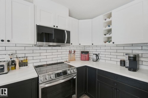 Two-tone cabinetry with white upper and dark lower cabinets, a subway tile backsplash, white countertops, and a stainless steel range with an over-the-range microwave - 38 Menalta Place, Cardiff, AB 