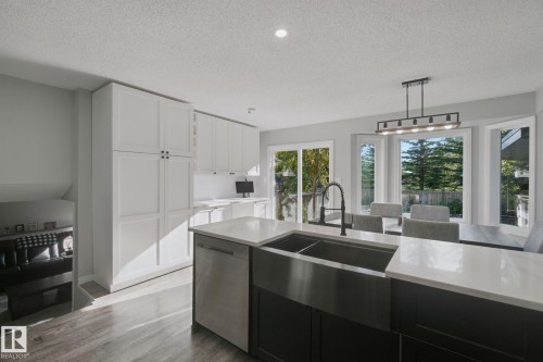 Spacious kitchen featuring white cabinetry, a large kitchen island with a dark basin sink, stainless steel dishwasher, and light countertops - 38 Menalta Place, Cardiff, AB 