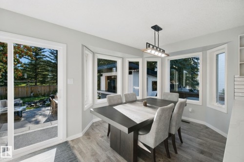 Dining area featuring wood-finish flooring, a contemporary chandelier, and a bay window with multiple panes - 38 Menalta Place, Cardiff, AB 