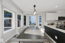 Open-concept kitchen and dining area featuring a modern black kitchen island, white upper cabinetry, subway tile backsplash, and light wood-finish flooring - 