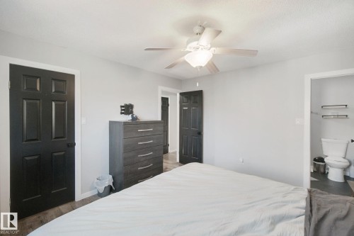 Light gray wall paint, wood-finish flooring, ceiling fan, six-panel interior doors, and a white toilet - 38 Menalta Place, Cardiff, AB 