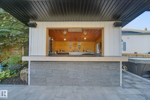 Outdoor bar structure featuring a stacked stone facade, white vertical siding, and a black soffit - 38 Menalta Place, Cardiff, AB 