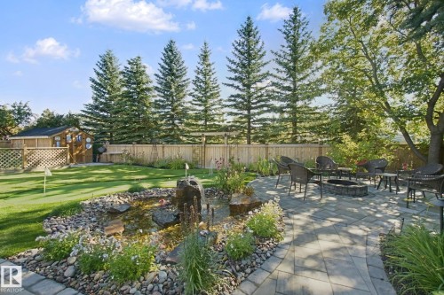 Expansive backyard featuring a paver patio with a built-in fire pit, a stone-lined pond with a water feature, a putting green, and tall evergreen trees along the perimeter - 38 Menalta Place, Cardiff, AB 
