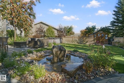 Manicured lawn with a decorative water feature, stone paver patio, and mature landscaping - 38 Menalta Place, Cardiff, AB 