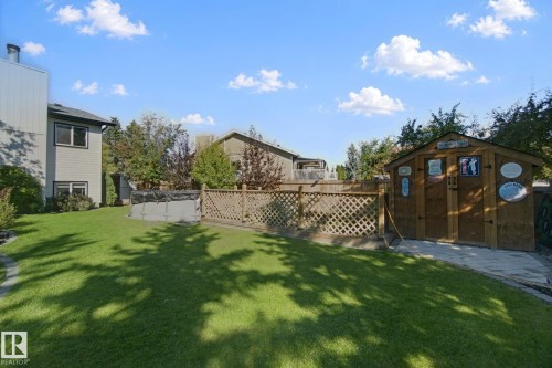 Expansive lawn area with a wooden lattice fence, wood storage shed, and a paved patio area - 38 Menalta Place, Cardiff, AB 