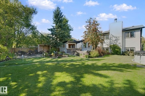 Expansive green lawn, putting green with multiple holes, established mature trees, stone patio area, and a wood privacy fence - 38 Menalta Place, Cardiff, AB 