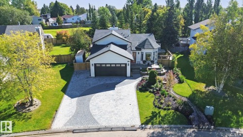 Gabled roofline, dark garage door, paved driveway, landscaped front yard, and mature trees - 38 Menalta Place, Cardiff, AB 