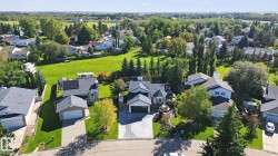 Residential property featuring an asphalt shingle roof, attached garage, and mature landscaping - 