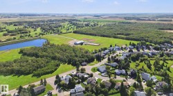 Residential community with a pond, surrounding green spaces, and mature tree lines - 