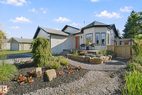 Exterior featuring a front patio, manicured landscaping with rock accents, gravel pathways, and an attached garage - 38 Menalta Place, Cardiff, AB 