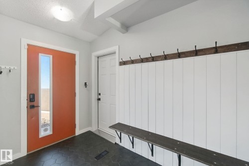 Entryway featuring a vibrant front door with vertical window, dark hexagon floor tiles, white wainscoting, and a built-in wooden bench with coat hooks - 38 Menalta Place, Cardiff, AB 