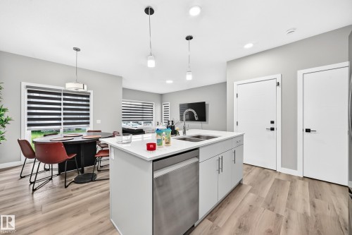 Kitchen island with integrated sink, stainless steel dishwasher, white shaker-style cabinetry, and light-toned wood-finish flooring - 2415 194 Street Nw, Edmonton, AB 