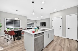 Kitchen island with integrated sink, stainless steel dishwasher, white shaker-style cabinetry, and light-toned wood-finish flooring - 