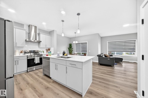 Modern kitchen featuring a central island with integrated sink, light-toned cabinetry, stainless steel appliances, and wood-finish flooring - 2415 194 Street Nw, Edmonton, AB 