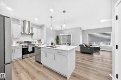Modern kitchen featuring a central island with integrated sink, light-toned cabinetry, stainless steel appliances, and wood-finish flooring - 