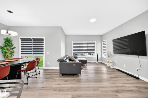 Spacious living area featuring wood-finish flooring, ample natural light, recessed ceiling lighting, and a modern dining pendant light - 2415 194 Street Nw, Edmonton, AB 