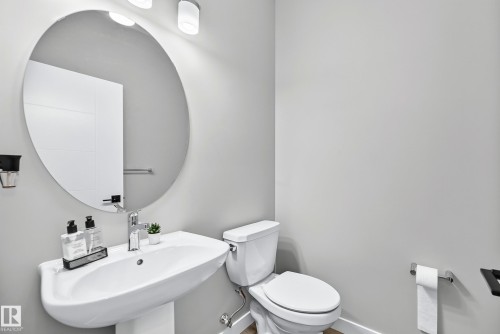 Pedestal sink with chrome faucet, circular wall-mounted mirror, and white toilet - 2415 194 Street Nw, Edmonton, AB 