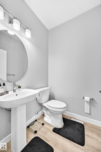 Pedestal sink with chrome faucet, circular wall mirror, track lighting fixture, and wood-finish flooring - 2415 194 Street Nw, Edmonton, AB 