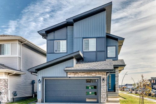 Modern architectural design with a multi-textured facade, stone accents, and a contrasting blue entry door - 2415 194 Street Nw, Edmonton, AB 
