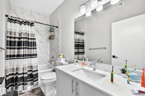 Modern bathroom featuring a single vanity with a white countertop and undermount sink, a large wall mirror, and a built-in bathtub with subway tile surround - 2415 194 Street Nw, Edmonton, AB 