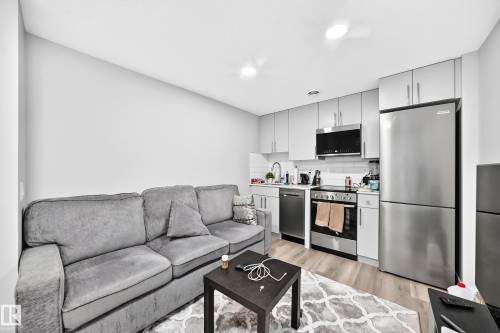 Galley kitchen with light gray cabinetry, stainless steel appliances, white subway tile backsplash, and wood-finish flooring - 2415 194 Street Nw, Edmonton, AB 