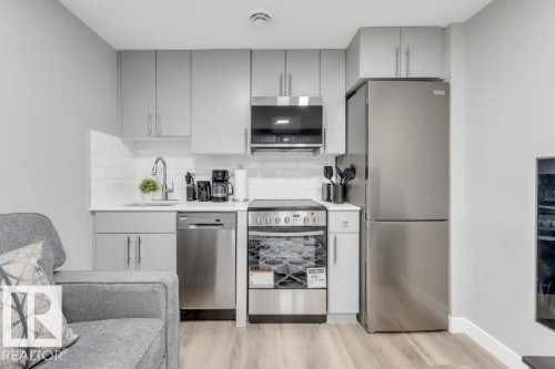 Kitchenette featuring gray cabinetry, white subway tile backsplash, stainless steel appliances, and wood-finish flooring - 2415 194 Street Nw, Edmonton, AB 