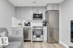 Kitchenette featuring gray cabinetry, white subway tile backsplash, stainless steel appliances, and wood-finish flooring - 