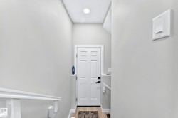 White panel door with black hardware, wood-finish flooring, and recessed ceiling lighting - 
