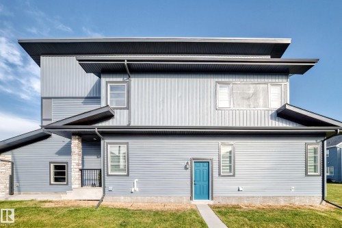 Contemporary exterior featuring a bright blue entry door, multi-level rooflines, corrugated and horizontal siding, and stone pillar accents - 2415 194 Street Nw, Edmonton, AB 
