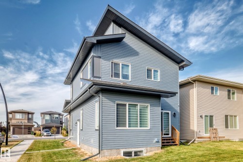 Modern exterior with blue horizontal siding, dark roofline, multiple windows, and a side entrance with wood stairs - 2415 194 Street Nw, Edmonton, AB 