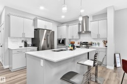 Kitchen featuring light-toned cabinetry, a central island with a sink, stainless steel appliances, a tile backsplash, and wood-finish flooring - 