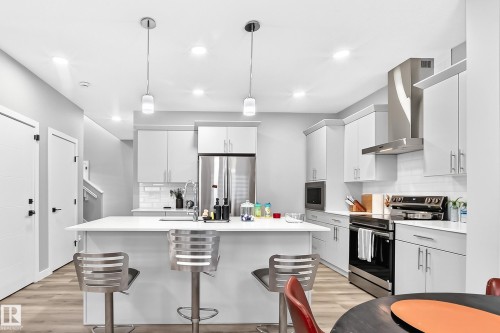 Modern kitchen featuring an island with seating, white shaker cabinetry, stainless steel appliances, and wood-finish flooring - 2415 194 Street Nw, Edmonton, AB 