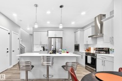 Modern kitchen featuring an island with seating, white shaker cabinetry, stainless steel appliances, and wood-finish flooring - 